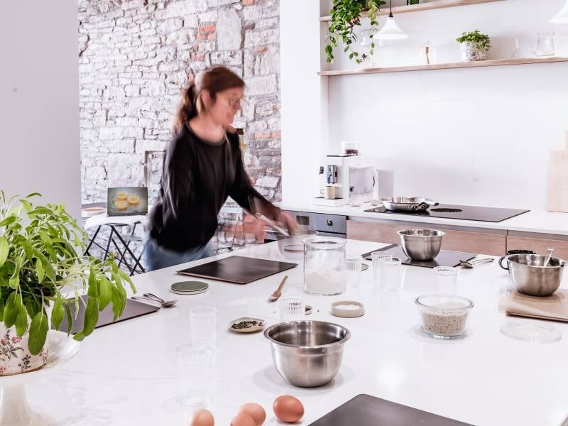 Personne en mouvement dans une cuisine moderne avec ingrédients et ustensiles sur un plan de travail blanc.
