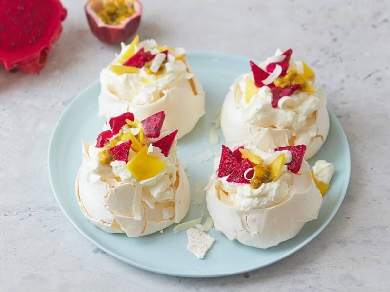 Quatre petites pavlovas garnies de fruits exotiques et de crème, présentées sur une assiette bleue lors d'un cours de pâtisserie à Dijon.