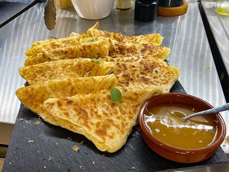 Assiette de crêpes dorées accompagnées d'une sauce dans un petit bol, présentées sur une ardoise noire.