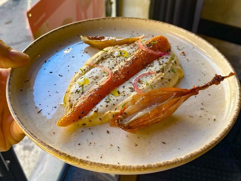 Plat gastronomique avec une carotte rôtie, une échalote et une purée, joliment dressé sur une assiette.
