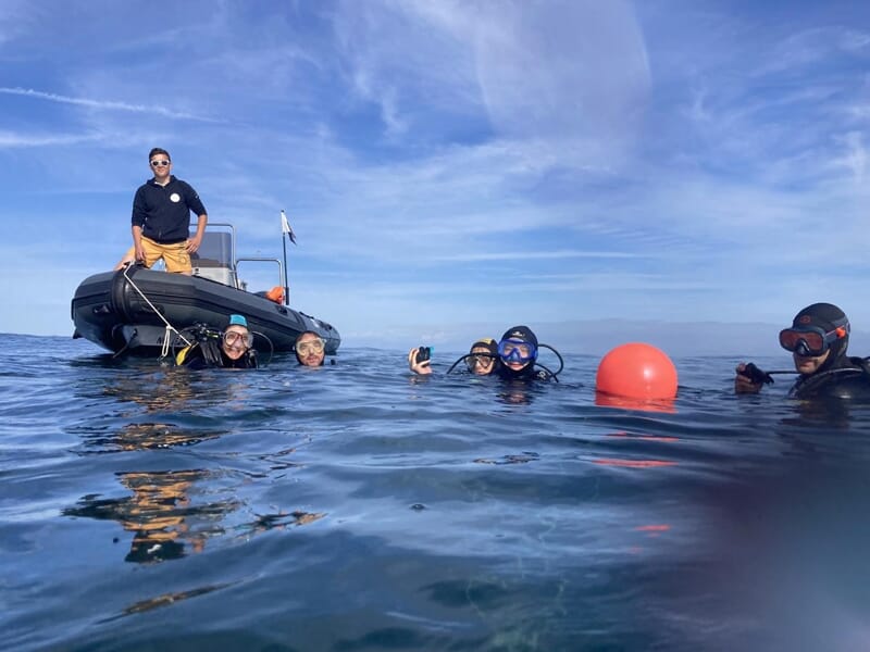 Groupe de plongeurs en surface près d'un bateau pneumatique sous un ciel bleu clair, prêts pour une plongée.