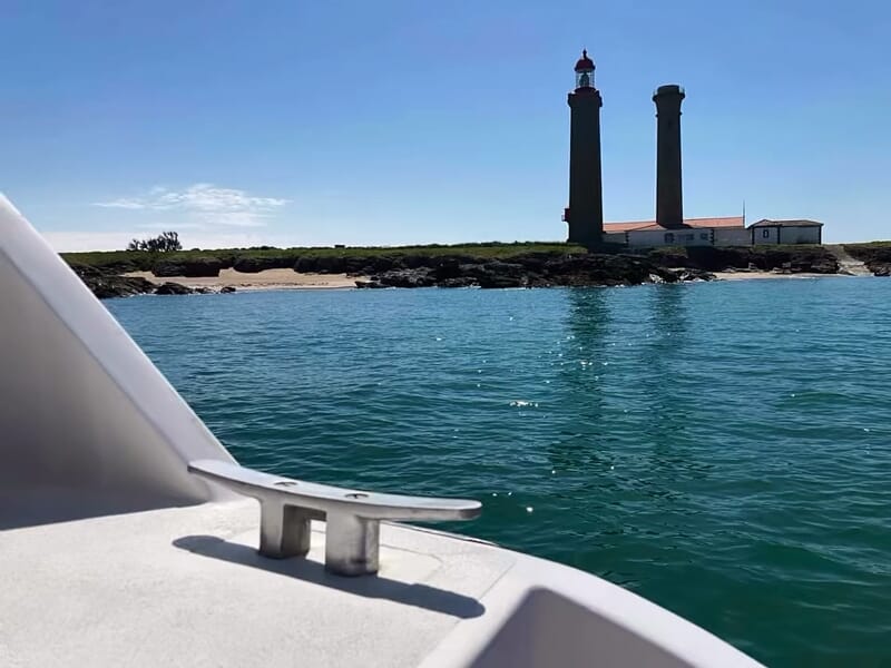 Vue depuis un bateau sur l'île de Noirmoutier avec deux phares et une mer calme sous un ciel bleu clair.