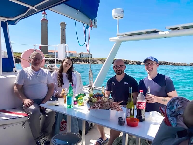 Quatre personnes souriantes à bord d'un bateau, dégustant un repas avec fruits de mer, face aux phares de Noirmoutier.