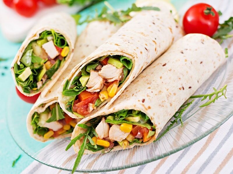 Trois wraps garnis de légumes frais et morceaux de poulet, présentés sur une assiette transparente.