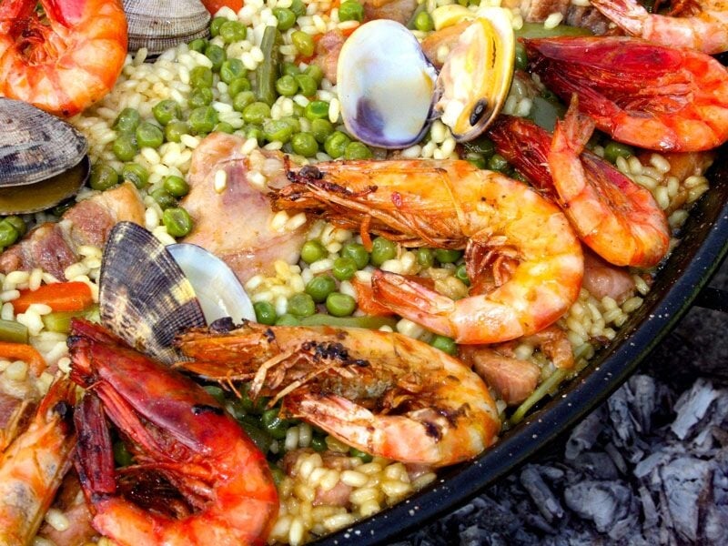 Plat de paella avec crevettes, moules, petits pois et riz, cuisiné dans une grande poêle noire.