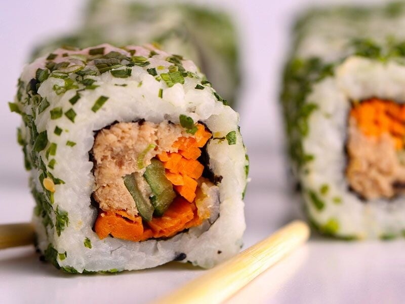 Sushi roulé avec riz, carottes, concombre et thon, décoré d'herbes vertes, accompagné de baguettes.