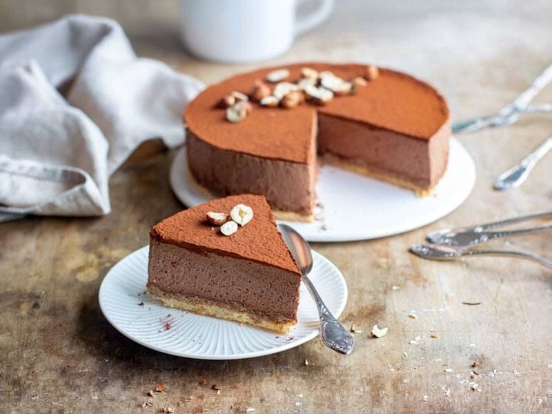 Gâteau au chocolat avec une tranche servie sur assiette blanche, décoré de noisettes et cacao.