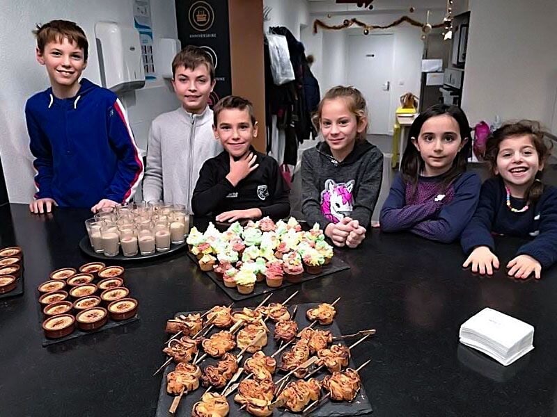 Six enfants souriants posent derrière une table avec des desserts variés lors d'un atelier culinaire.