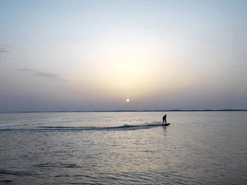 Surfeur électrique naviguant sur une mer tranquille avec le soleil bas à l'horizon à Andernos-les-Bains.
