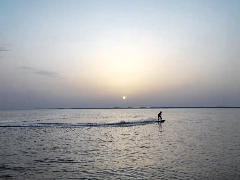 Surfeur électrique naviguant sur une mer tranquille avec le soleil bas à l'horizon à Andernos-les-Bains.