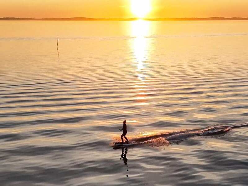 Surfeur électrique silhouetté sur l'eau au coucher du soleil avec reflet doré à Andernos-les-Bains.