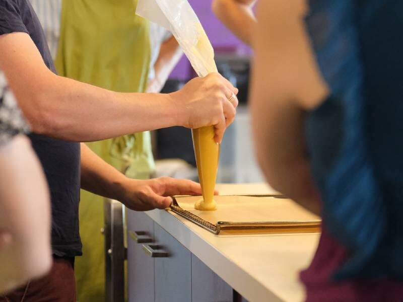 Personne en train de décorer une pâtisserie avec une poche à douille dans un cours de cuisine à Beaucouzé.