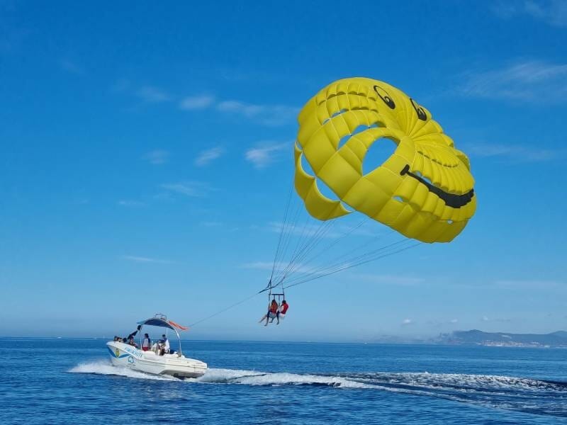 Parachute ascensionnel avec voile jaune souriante au-dessus de la mer, tracté par un bateau blanc à Saint-Cyr-sur-Mer.