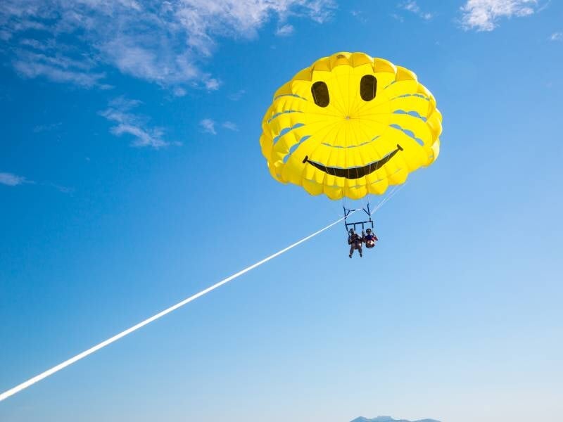 Deux personnes en parachute ascensionnel sous une voile jaune souriante, tirées par un bateau sur une mer calme.