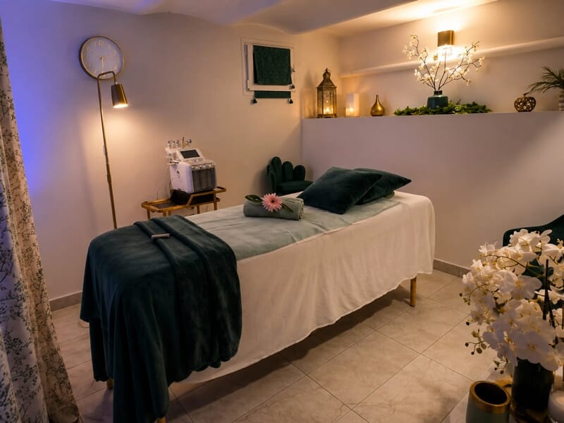 Table de massage avec draps verts dans une salle apaisante décorée de plantes et d'objets zen.