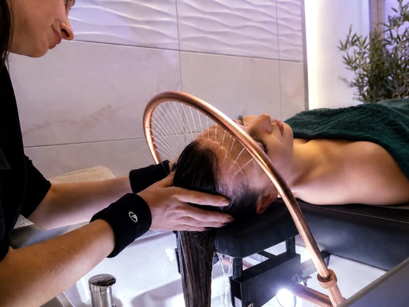 Personne recevant un soin capillaire avec un professionnel dans un environnement relaxant et moderne.
