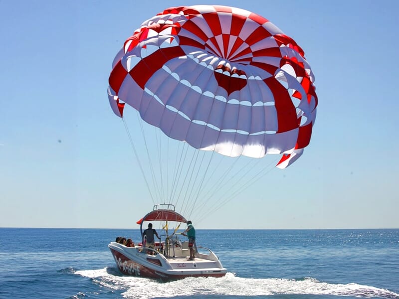 Bateau blanc avec parachute ascensionnel rouge et blanc sur la mer calme sous un ciel bleu clair.