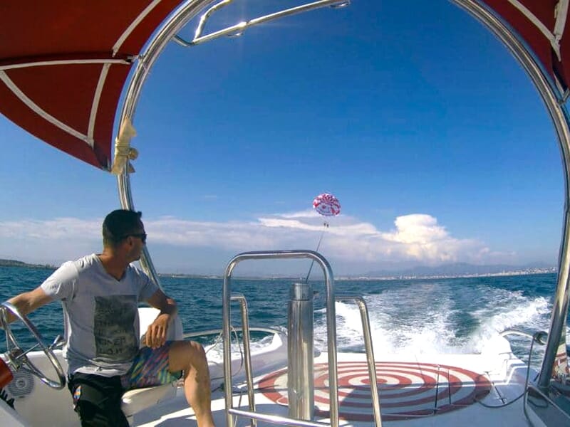 Homme assis sur un bateau regardant un parachute ascensionnel rouge et blanc au loin sur la mer.