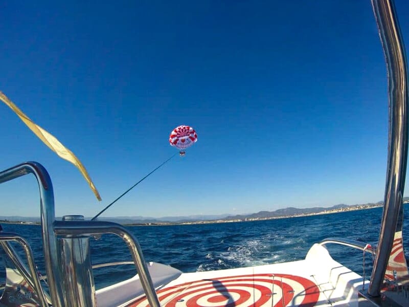 Vue depuis un bateau avec un parachute ascensionnel rouge et blanc tiré sur la mer et ciel bleu.