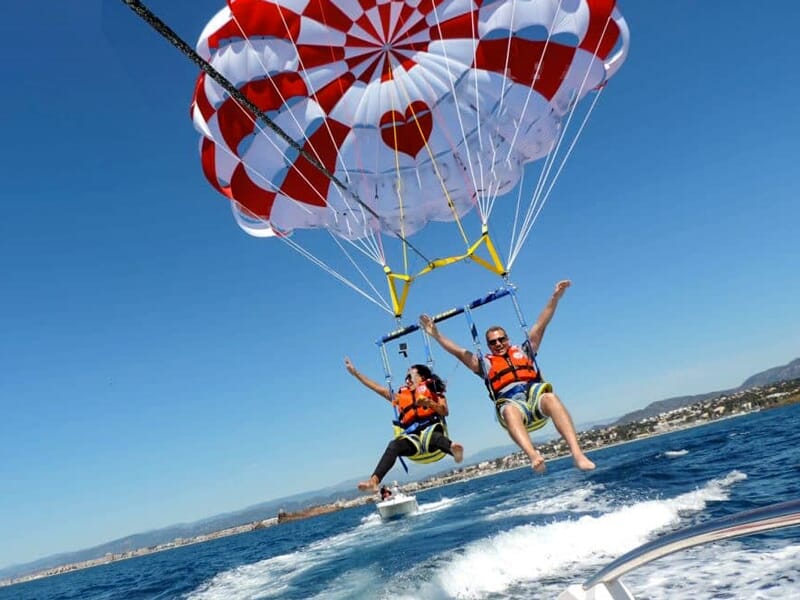 Deux personnes en gilets de sauvetage volent en parachute ascensionnel rouge et blanc au-dessus de la mer.