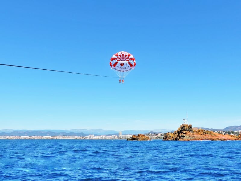 Deux personnes en parachute ascensionnel au-dessus de la mer bleue près d'une côte rocheuse sous un ciel clair.