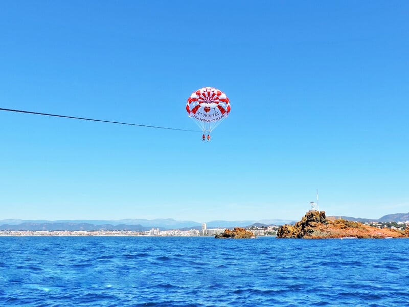 Deux personnes en parachute ascensionnel au-dessus de la mer bleue près d'une côte rocheuse sous un ciel clair.