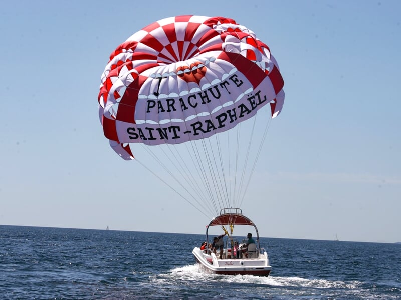 Bateau tirant un parachute ascensionnel rouge et blanc avec l'inscription 'Saint-Raphaël' sur la mer calme.