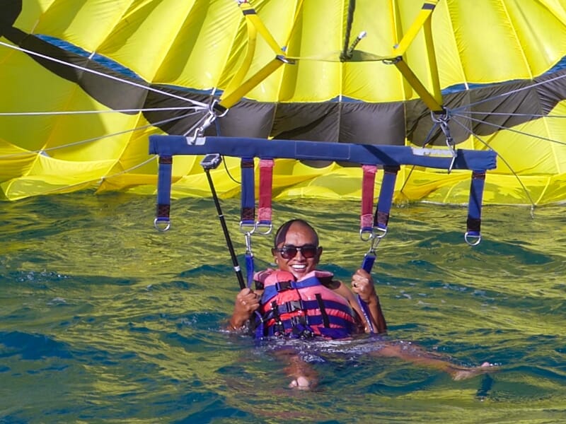 Personne souriante en parachute ascensionnel avec un parachute jaune au-dessus de l'eau bleue claire.