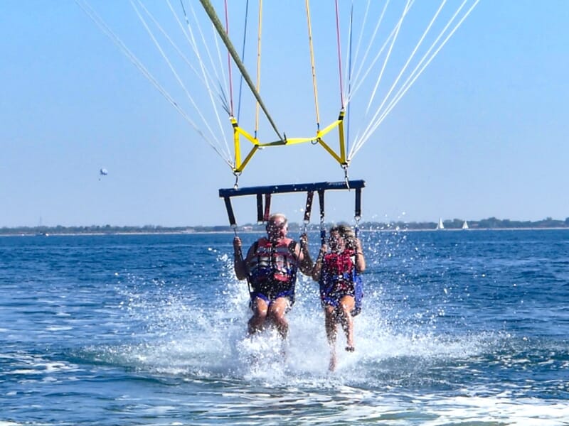 Deux personnes en parachute ascensionnel touchant l'eau en même temps, tirées par un bateau sur la mer.