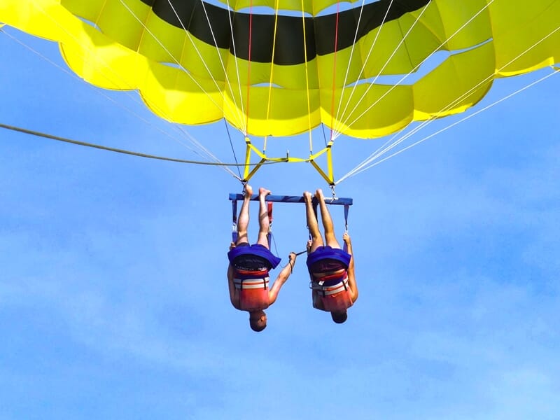 Deux personnes suspendues en parachute ascensionnel, vues de dos, avec un ciel bleu clair en arrière-plan.