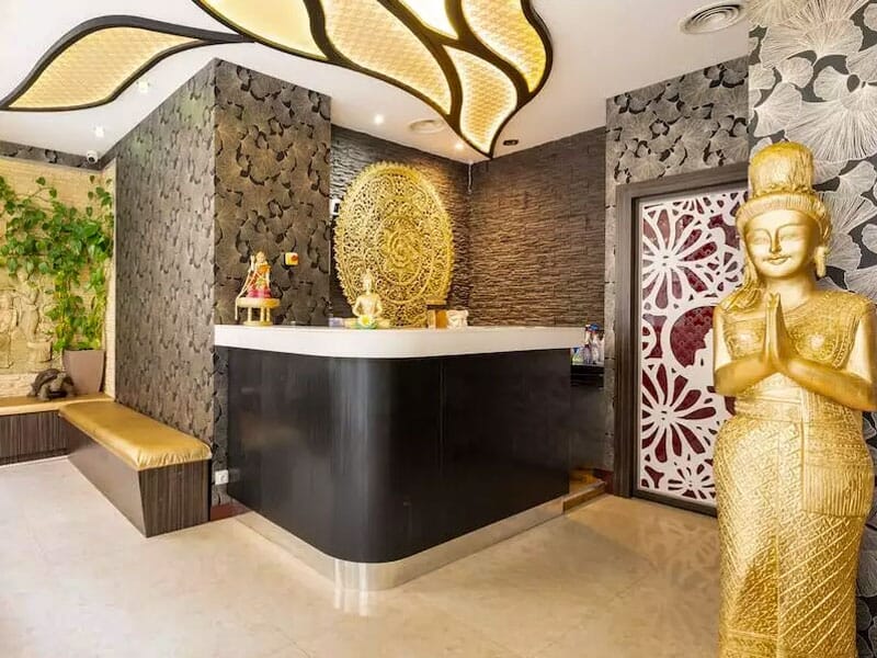 Intérieur d'un spa avec comptoir noir, statue dorée en prière et décoration murale zen et végétale.
