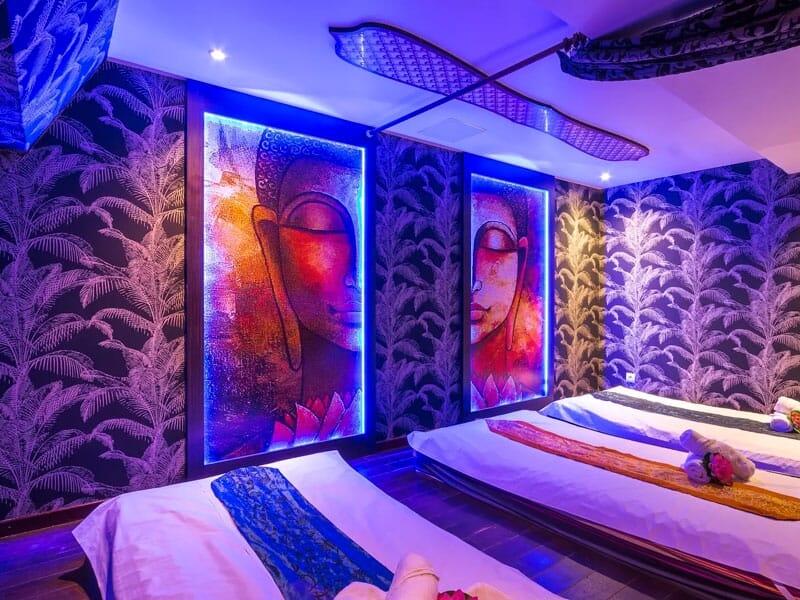 Salle de massage avec deux tables, éclairage bleu, décorations murales artistiques et ambiance relaxante.