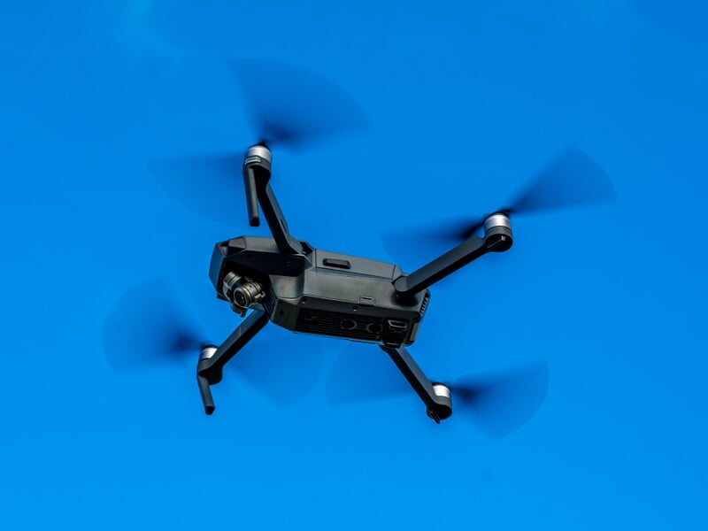 Drone noir en vol avec ses hélices en mouvement sur un ciel bleu clair sans nuages en arrière-plan.
