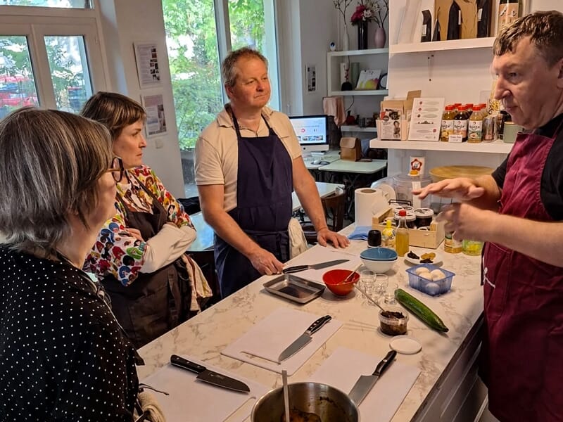 Cours de cuisine avec un chef expliquant une recette à trois participants attentifs dans une cuisine moderne.