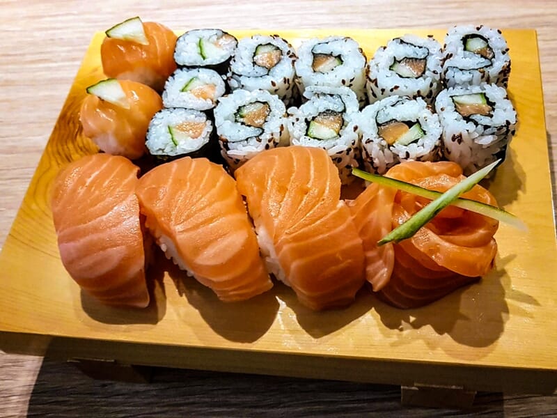 Plateau en bois avec assortiment de sushi et maki au saumon, joliment présentés sur une table.
