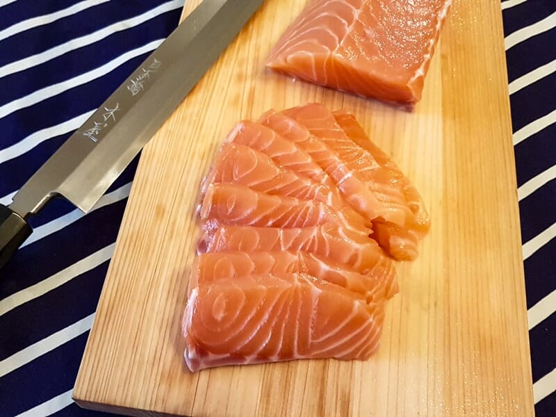Filets de saumon frais tranchés sur une planche en bois avec un grand couteau japonais à côté.