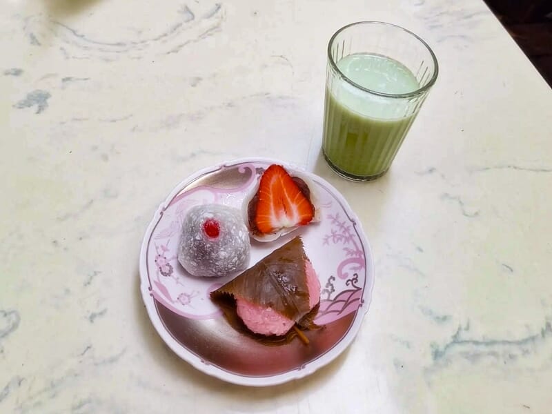 Assiette avec un mochi blanc, une fraise coupée en deux et un gâteau au chocolat sur une table claire.