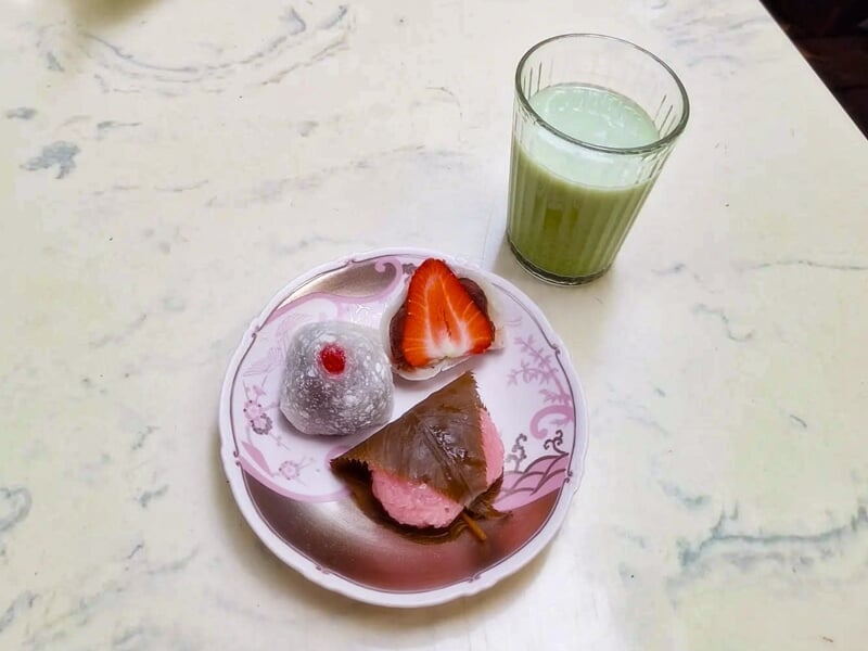 Assiette avec un mochi blanc, une fraise coupée en deux et un gâteau au chocolat sur une table claire.