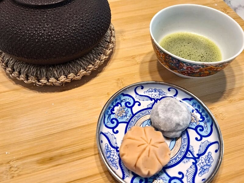 Tasse de thé vert et assiette bleue avec deux pâtisseries japonaises sur un plateau en bois clair.