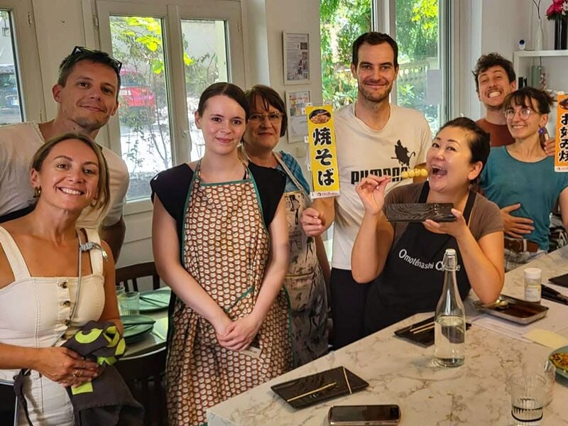 Groupe de personnes souriantes dans une cuisine, participant à un cours de cuisine à Lyon, ambiance conviviale.