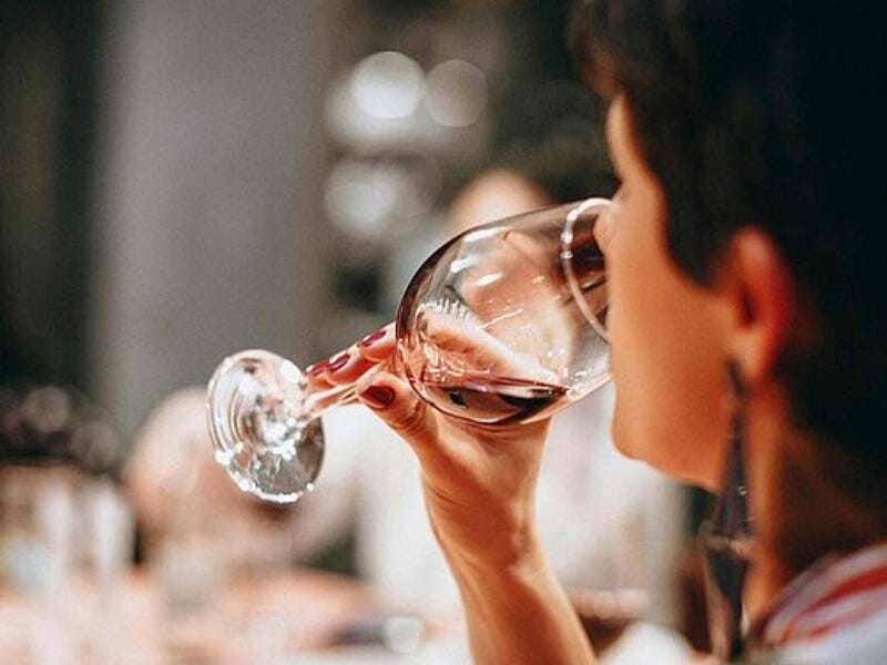 Personne dégustant un verre de vin rouge dans une ambiance chaleureuse et conviviale lors d'un repas.