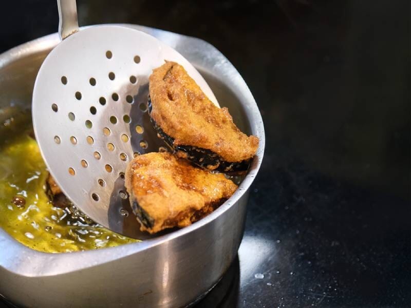 Deux morceaux de poisson pané en train de frire dans une casserole d'huile chaude avec une écumoire.