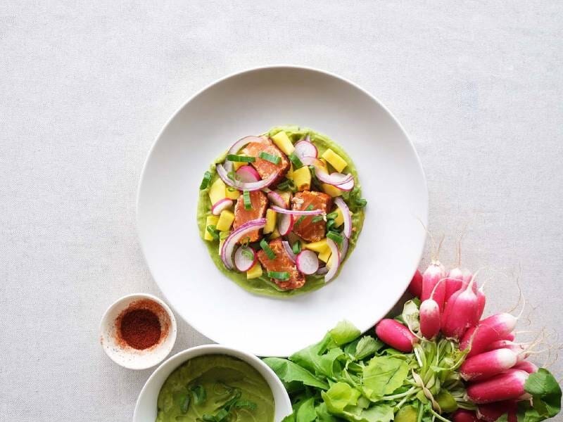 Plat coloré avec légumes frais, radis, avocat et sauce verte, accompagné de radis entiers.