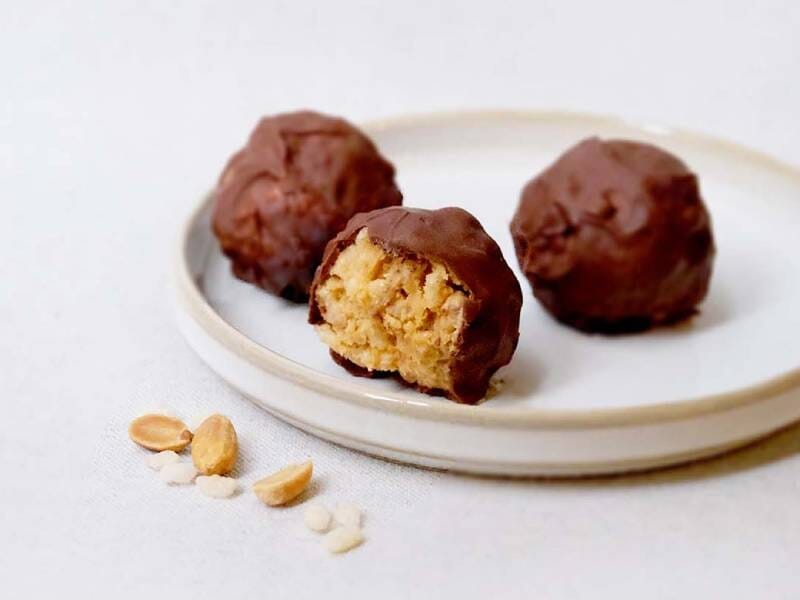 Trois boules de chocolat avec une à moitié mangée, posées sur une assiette blanche avec des cacahuètes à côté.