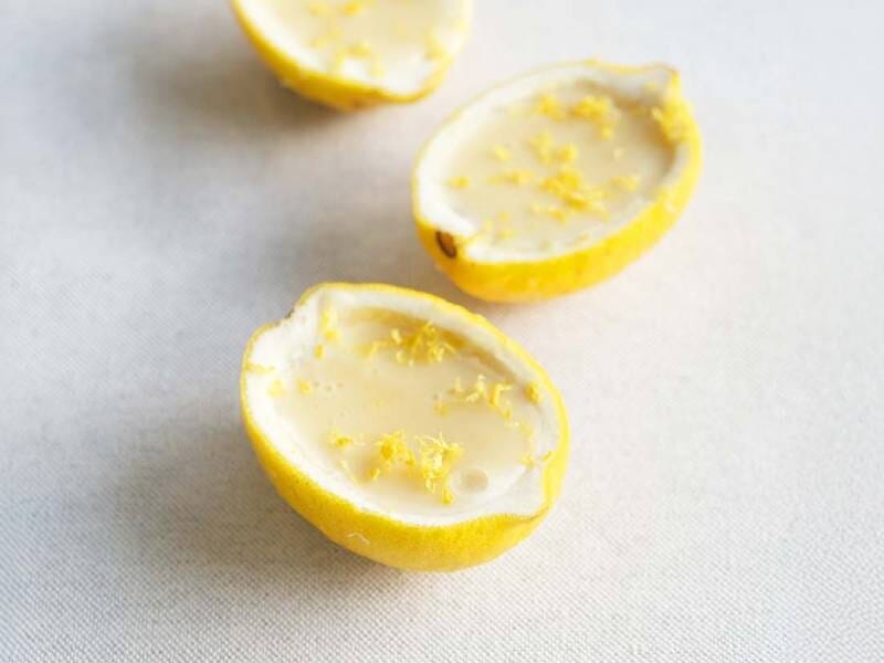 Deux moitiés de citron évidées avec du zeste râpé à l'intérieur, posées sur une surface claire.