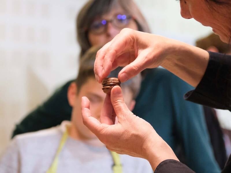 Une main tient un petit gâteau au chocolat devant un groupe de personnes attentives lors d'un atelier.