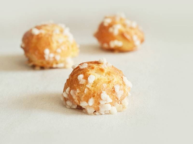 Trois chouquettes posées sur une surface claire, avec des grains de sucre visibles sur le dessus.