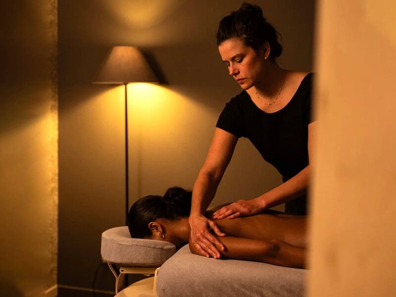 Une femme masse le dos d'une autre personne allongée sur une table de massage dans une pièce tamisée.