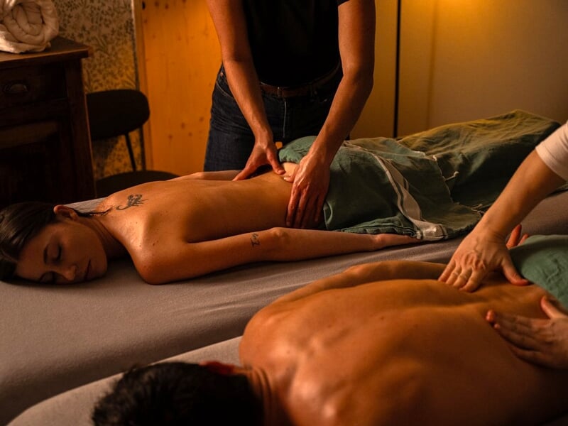 Deux personnes reçoivent un massage du dos simultanément dans une pièce chaleureuse et tamisée.