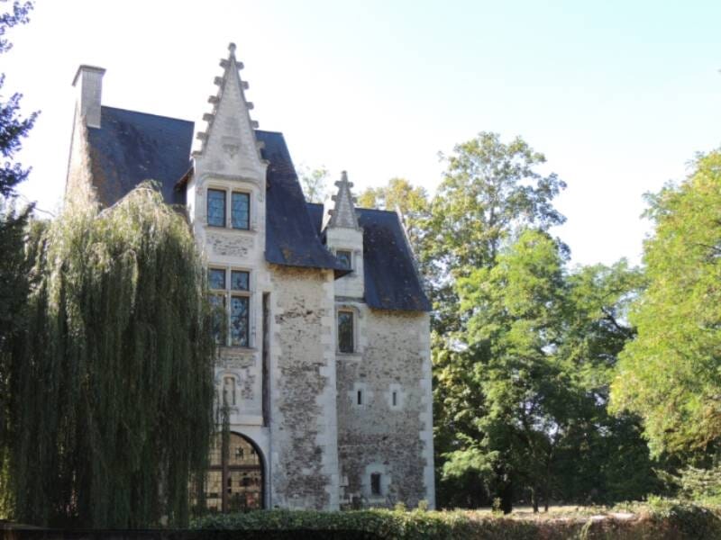 Vue d'un vieux manoir en pierre avec un toit en ardoise et un grand saule pleureur à gauche
